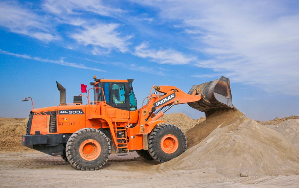 pexels-photo-1116035-1116035 An orange bulldozer at work, moving sand under a clear blue sky on a construction site.